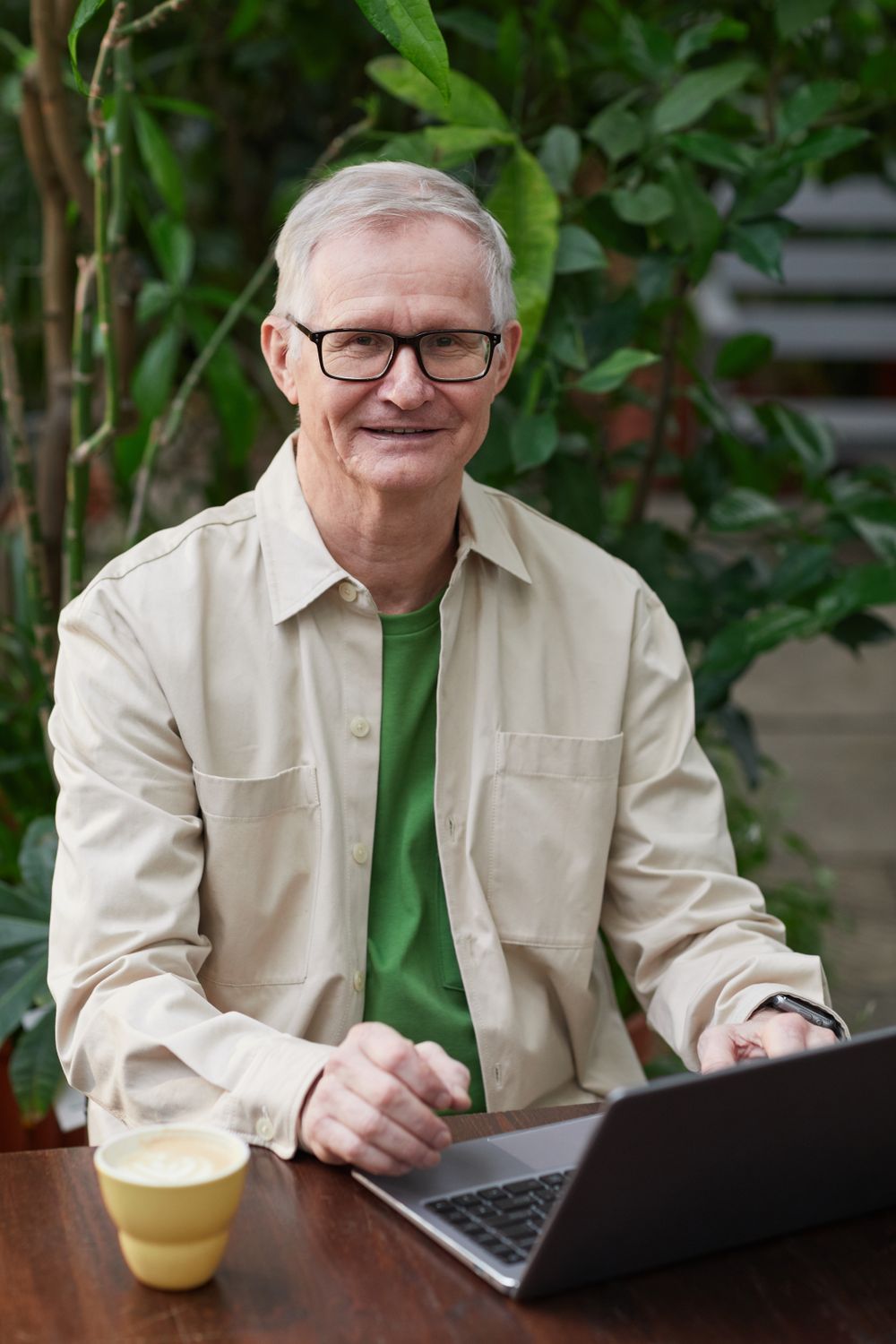 A smiling older man at a cafe table with his laptop, ready for his setup call