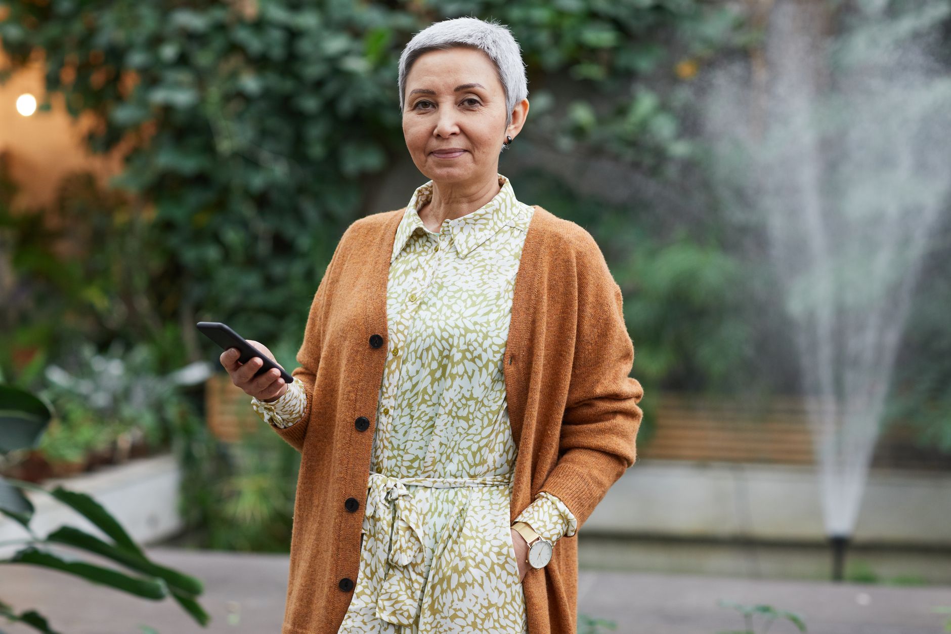 Best Cheap Phones for Seniors on a Fixed Income Senior woman with short hair using smartphone in an indoor greenhouse.