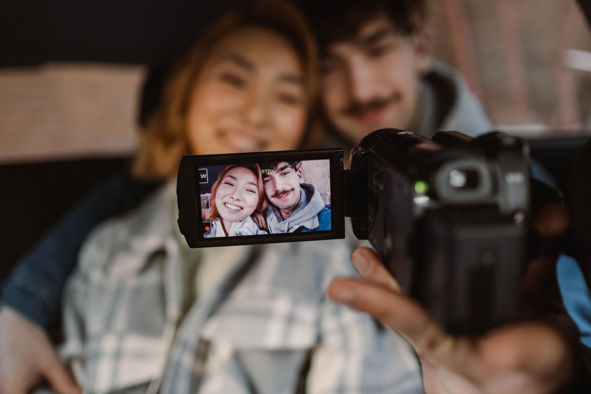 A couple films themselves with a video camera, capturing a joyful moment indoors.