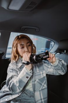 Woman in plaid jacket using camcorder inside car interior, showcasing technology usage.
