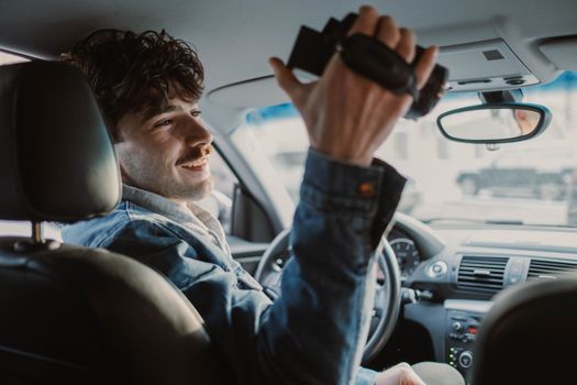 A young man smiling and holding a camcorder while inside a car, capturing moments.