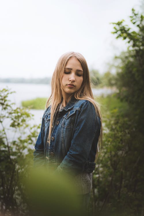 Dreamy young woman standing in green nature near pond