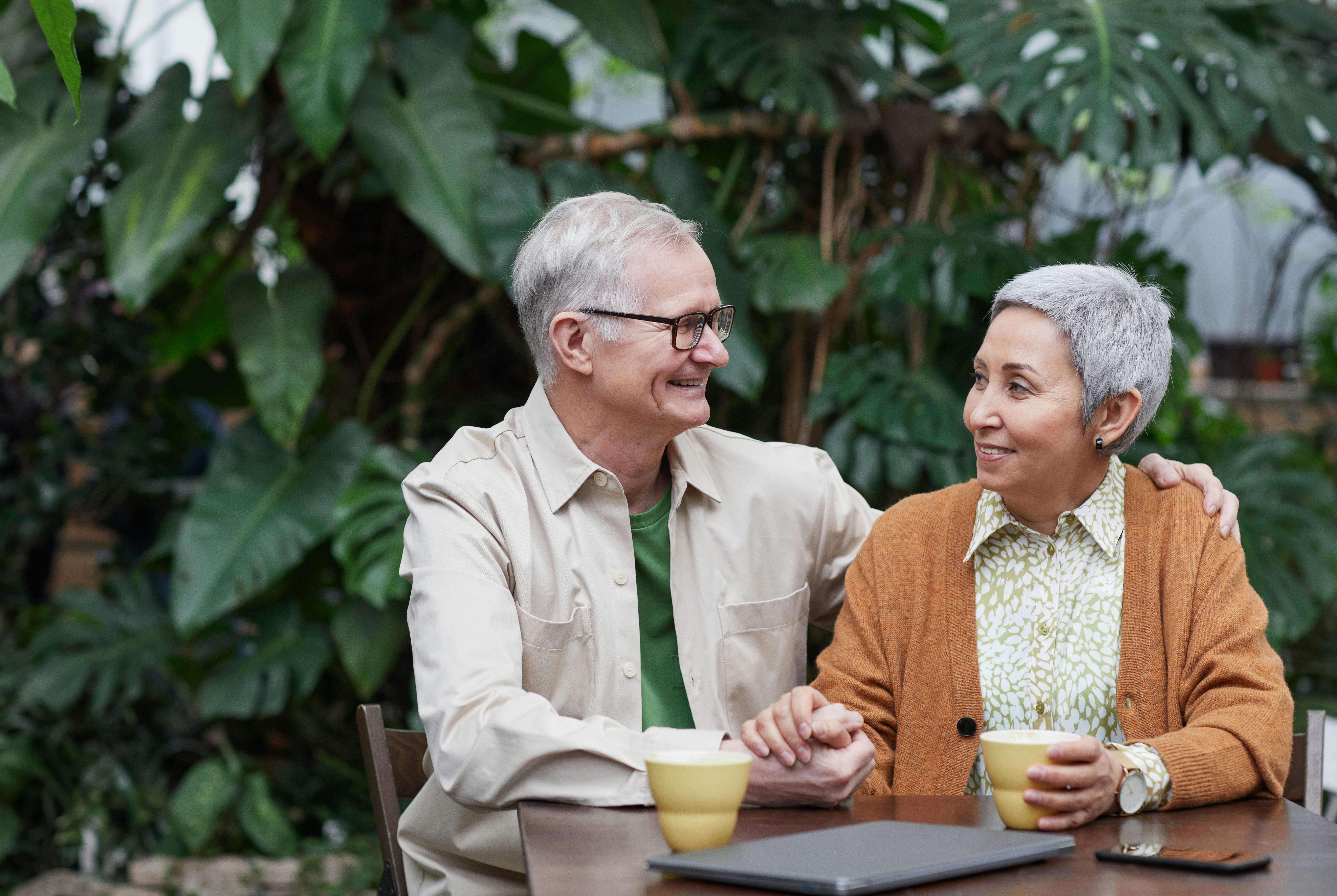 A cheerful elderly couple sharing coffee and affection at a rustic outdoor setting.
