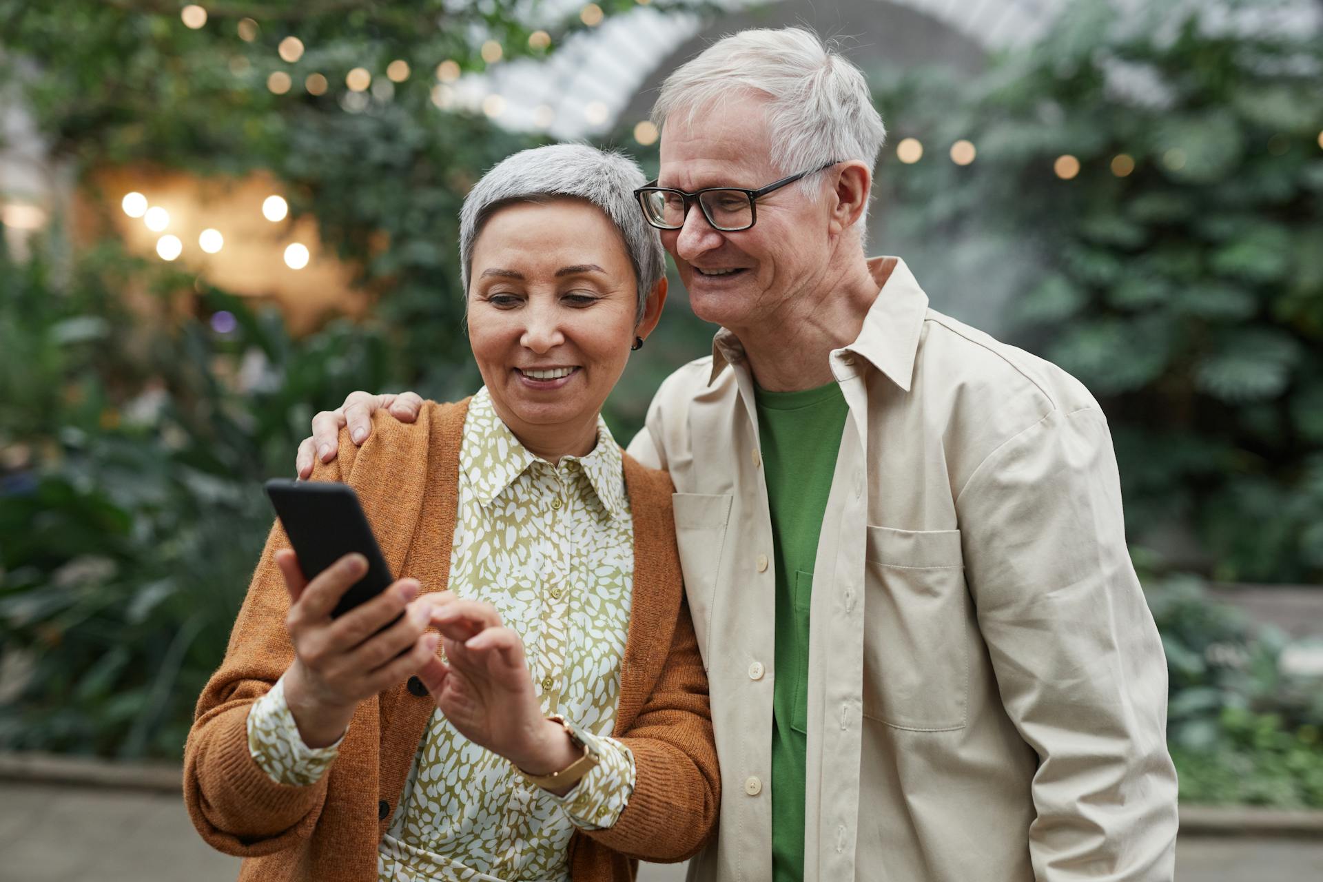 Happy senior couple using a smartphone together outdoors, expressing joy and connection.