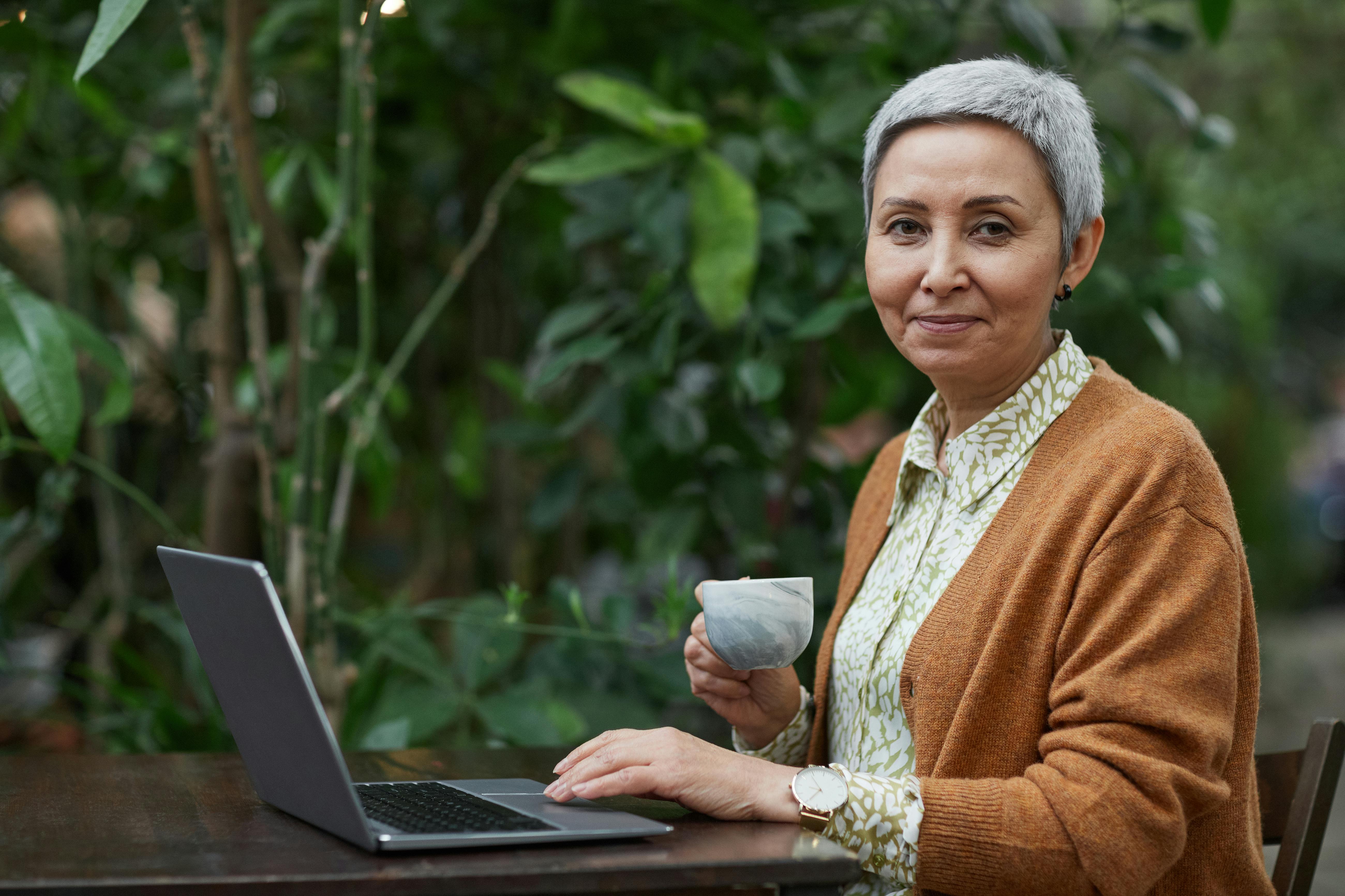 woman using her laptop while holding a coffee cup
