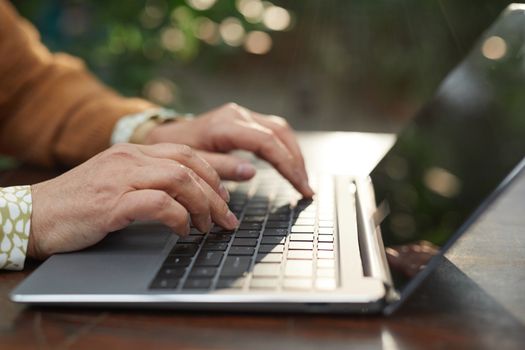 Close-up of hands typing on a laptop outdoors with natural background and sunlight.