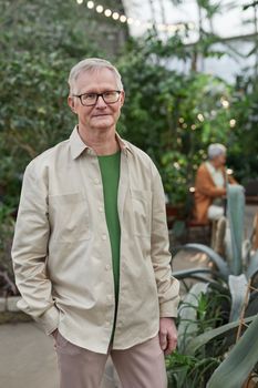 Portrait of a senior man standing in a lush indoor garden, smiling confidently.