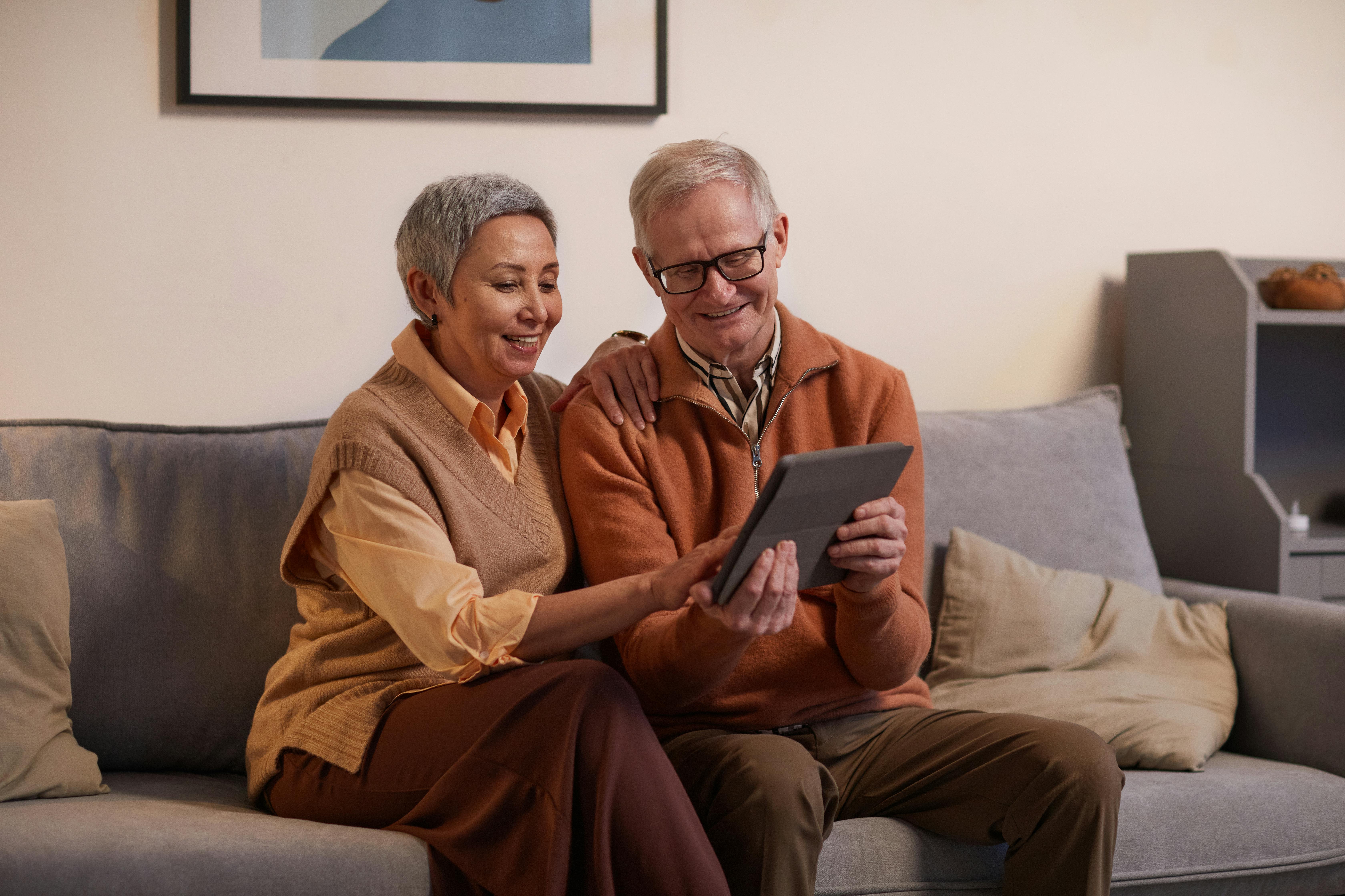 man and woman sitting on sofa while looking at a tablet computer