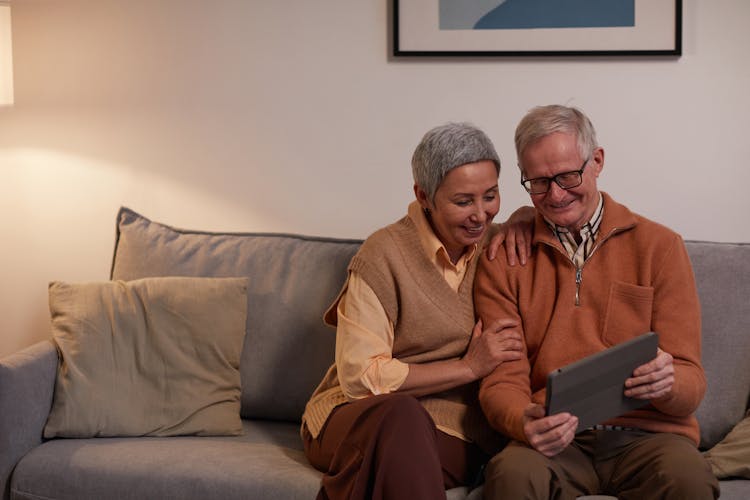 Man And Woman Sitting On Sofa While Looking At A Tablet Computer