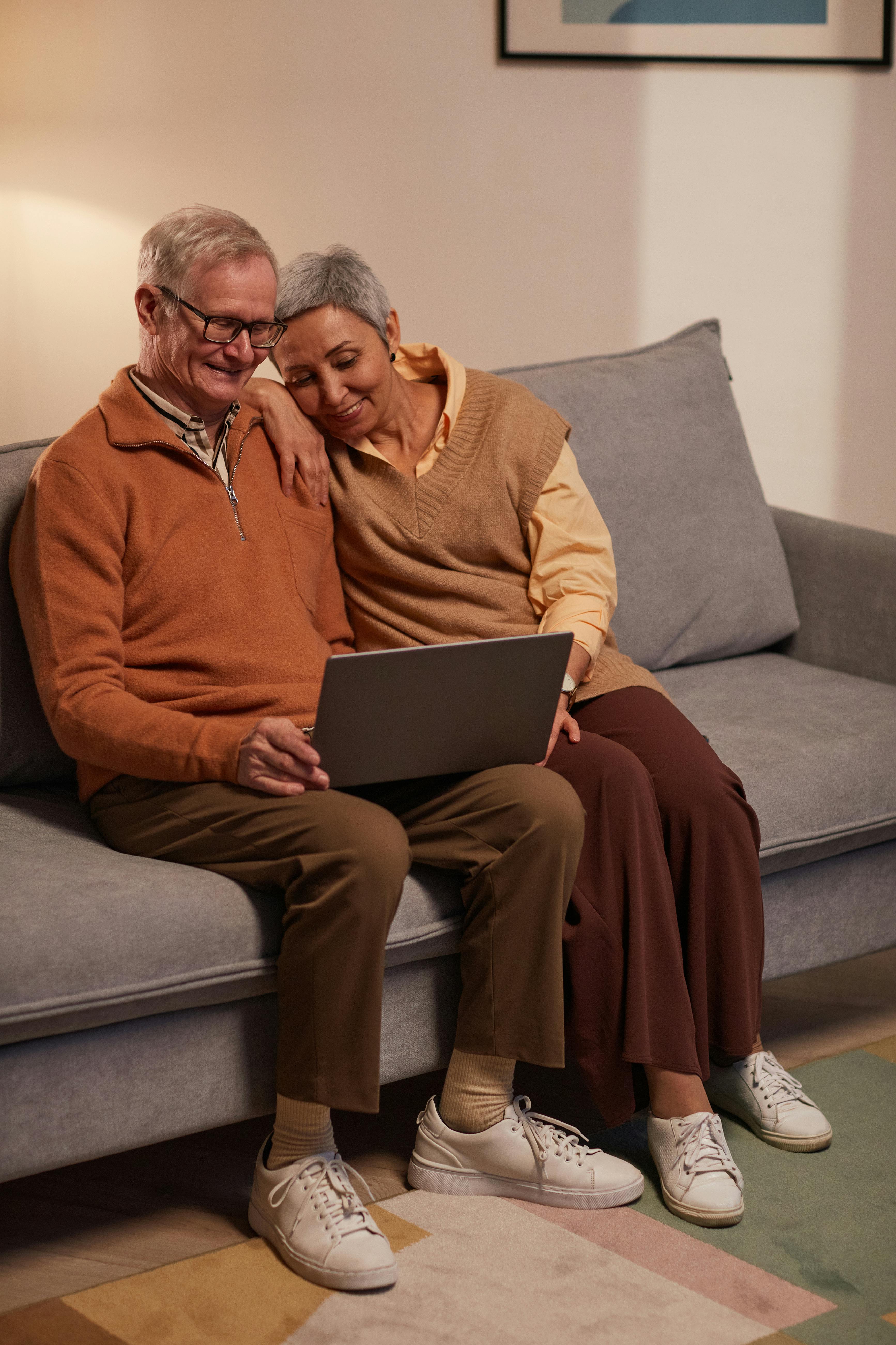 man and woman sitting on sofa while looking at a laptop