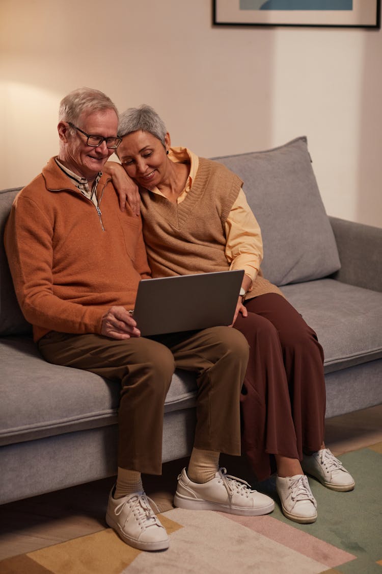 Man And Woman Sitting On Sofa While Looking At A Laptop