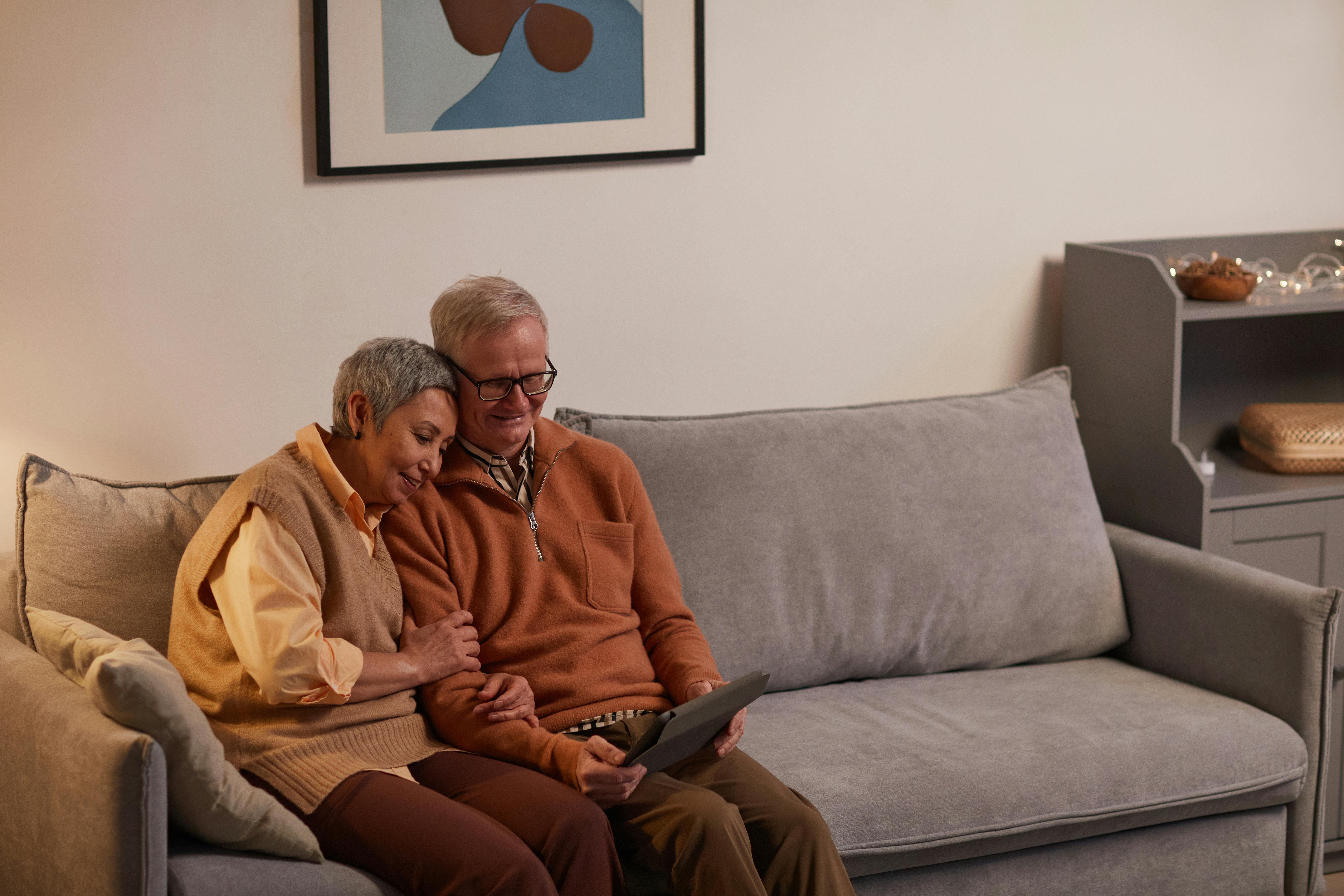 man and woman sitting on sofa while looking at a tablet computer