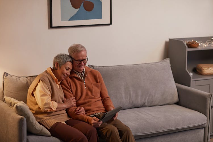 Man And Woman Sitting On Sofa While Looking At A Tablet Computer