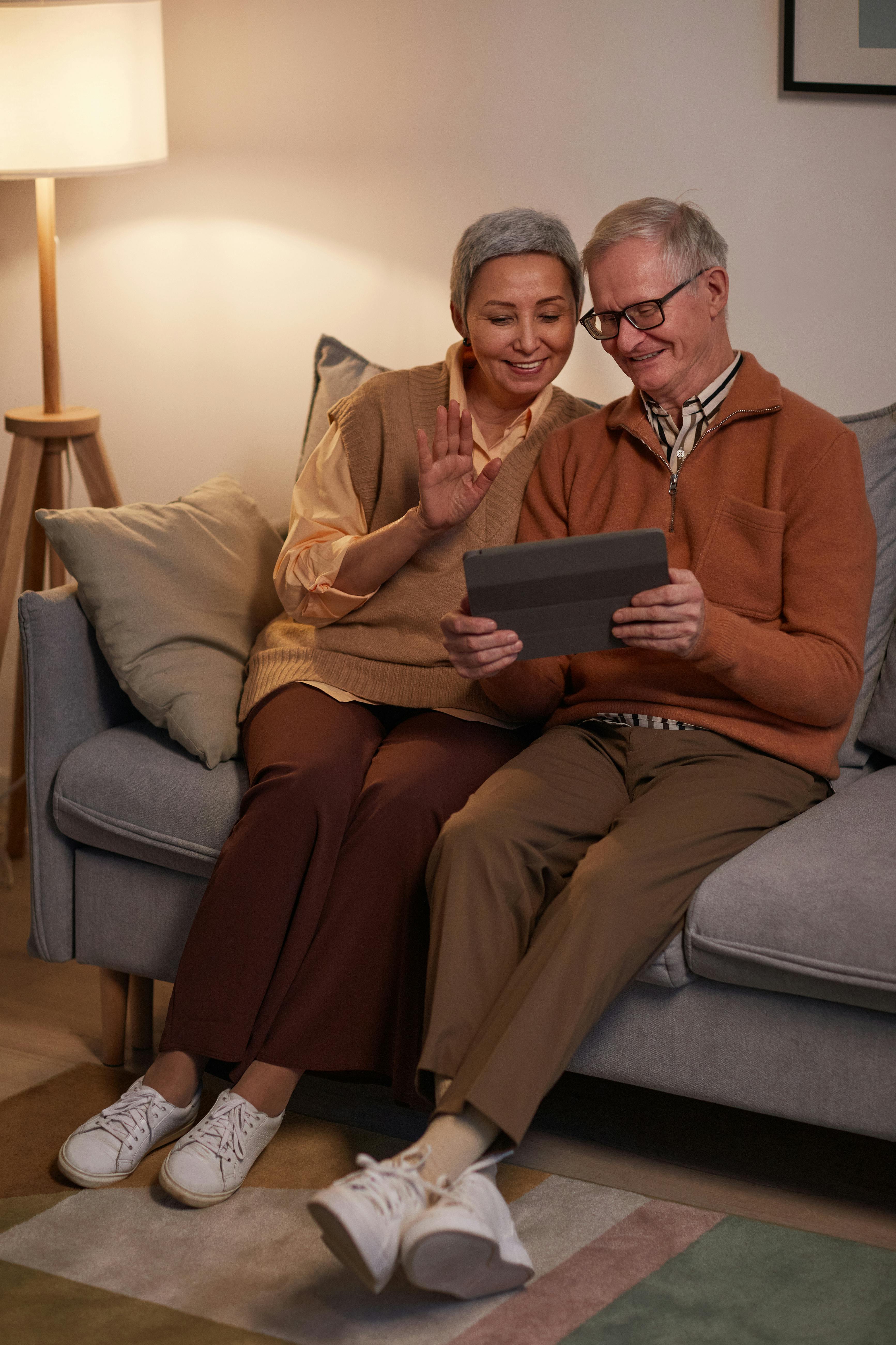 man and woman sitting on sofa while looking at a tablet computer