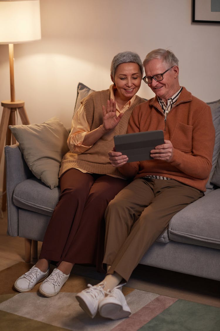 Man And Woman Sitting On Sofa While Looking At A Tablet Computer