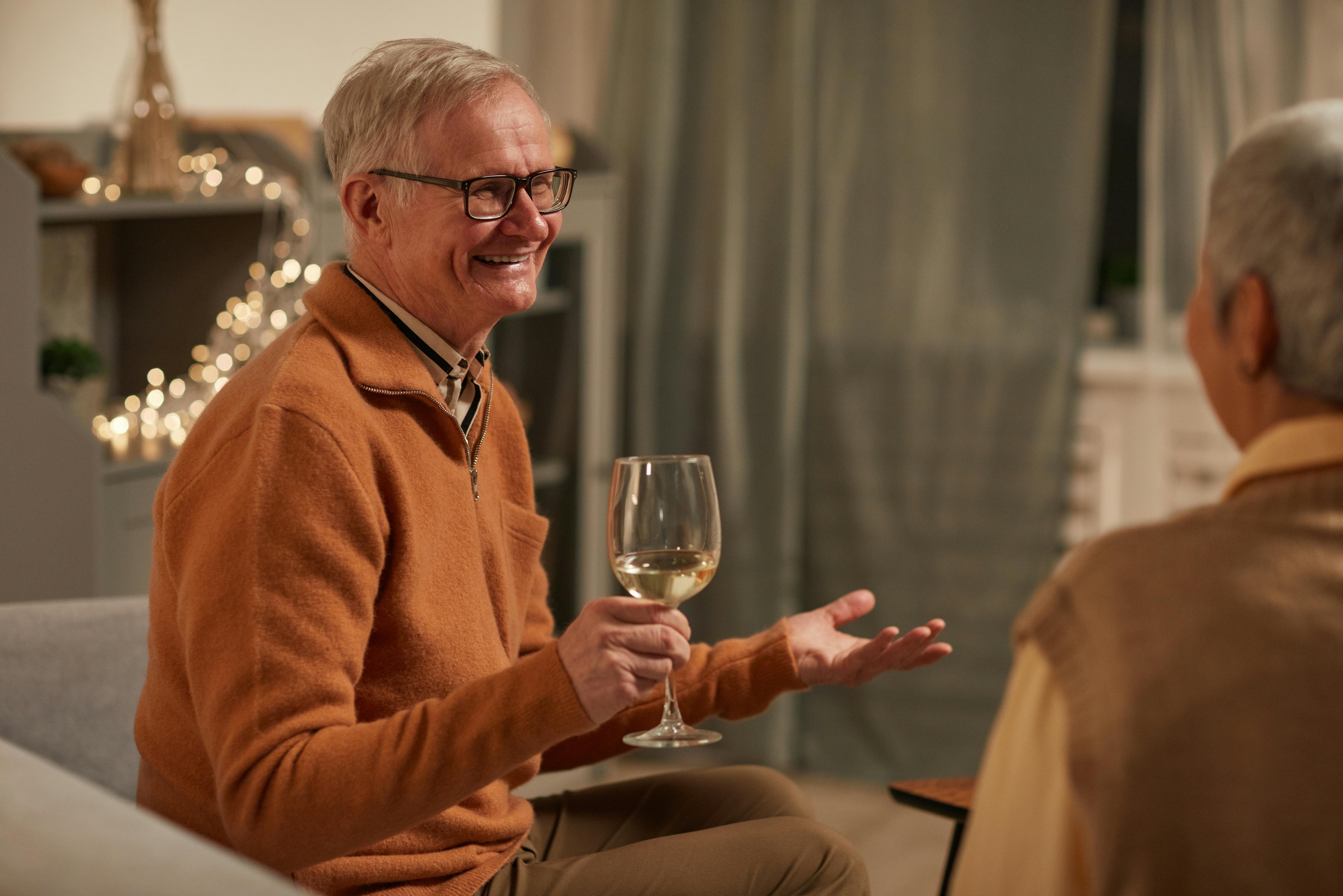 man in brown sweater smiling while holding wine glass