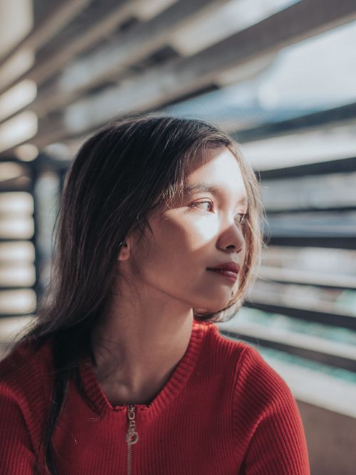 Free Portrait of a young woman gazing out a window with sunlight casting shadows over her face. Stock Photo