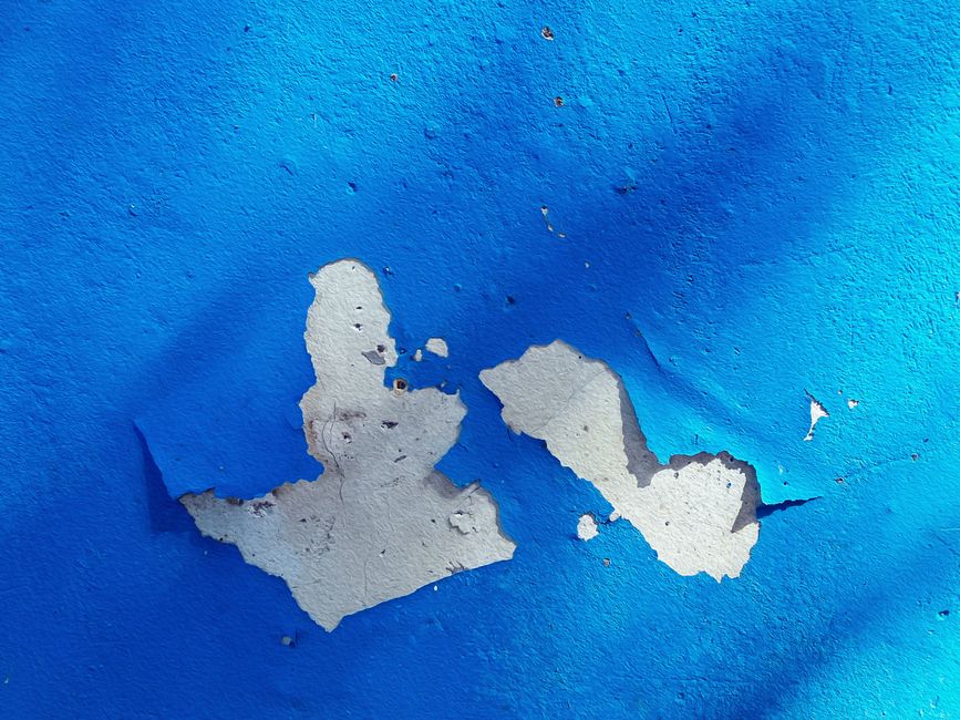 Close-up of a blue wall with peeling paint, showcasing texture and color contrast.