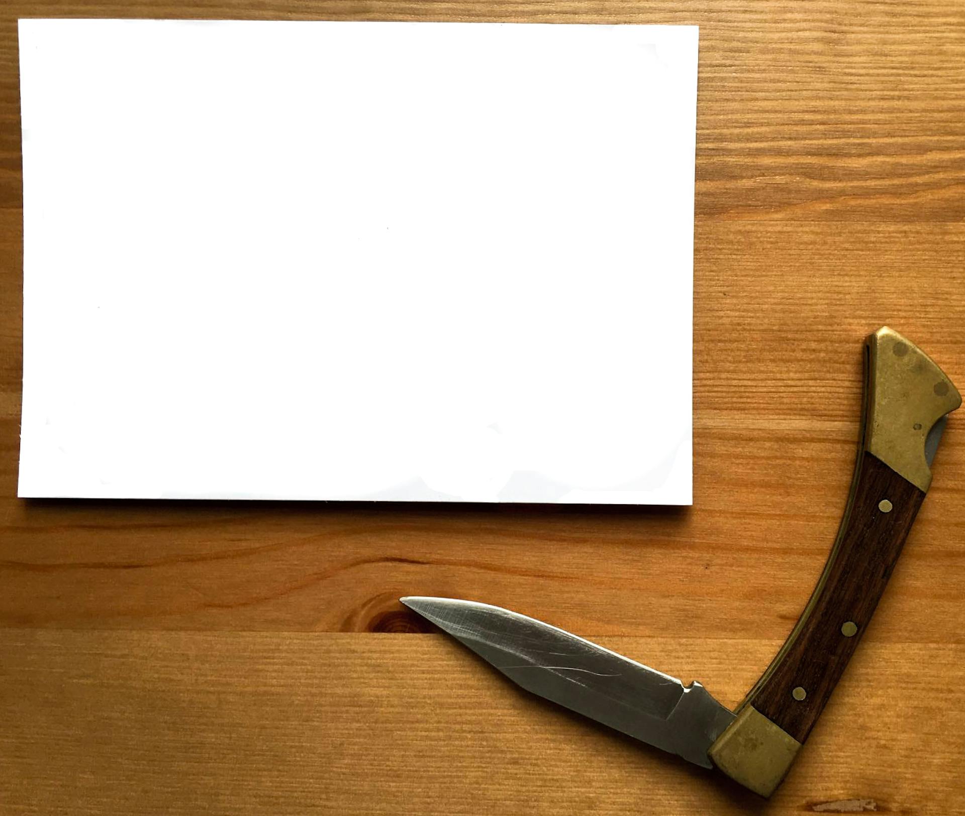 A simple flat lay of a pocket knife and blank paper on a wooden desk, offering copyspace.