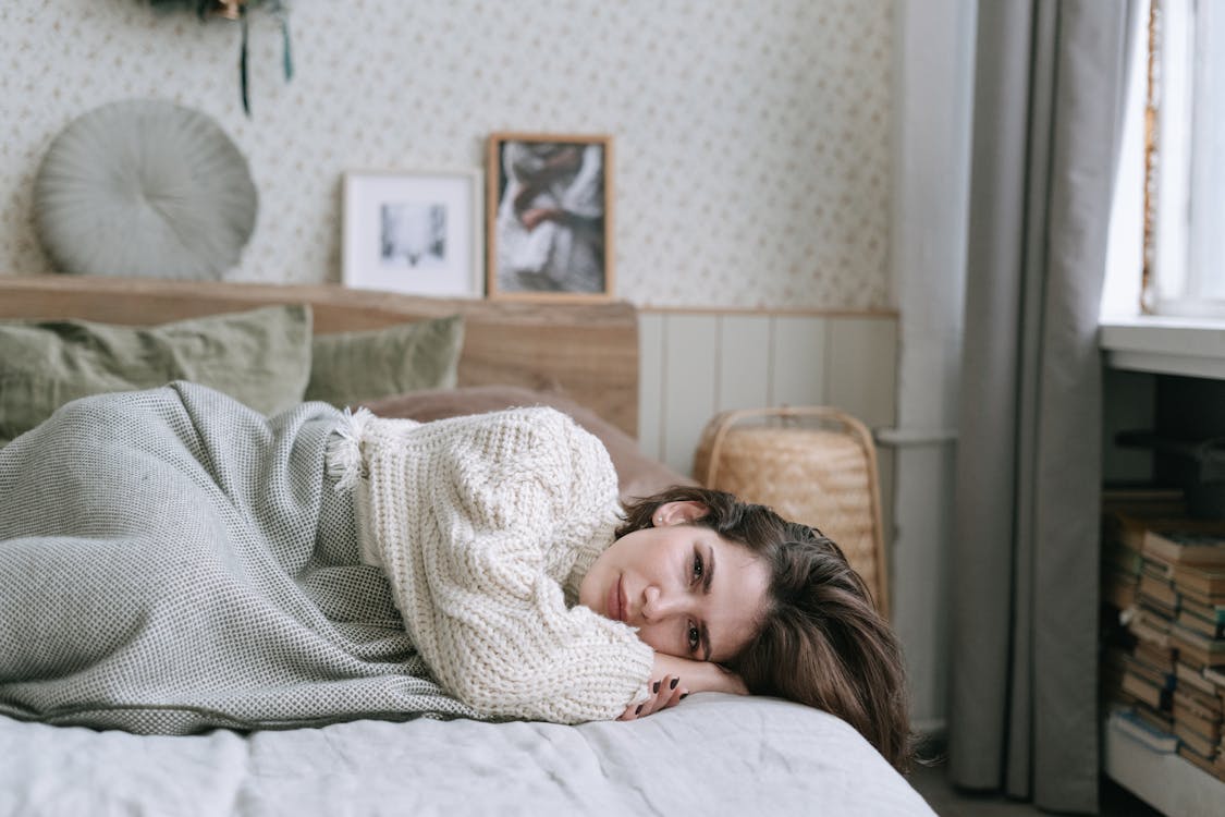 Free A Woman in White Knitted Sweater Lying on the Bed Stock Photo