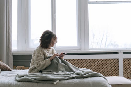 Woman in White Knit Sweater Sitting on Bed