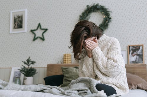 Free A Woman Sitting on a Bed and Covering Her Face Stock Photo