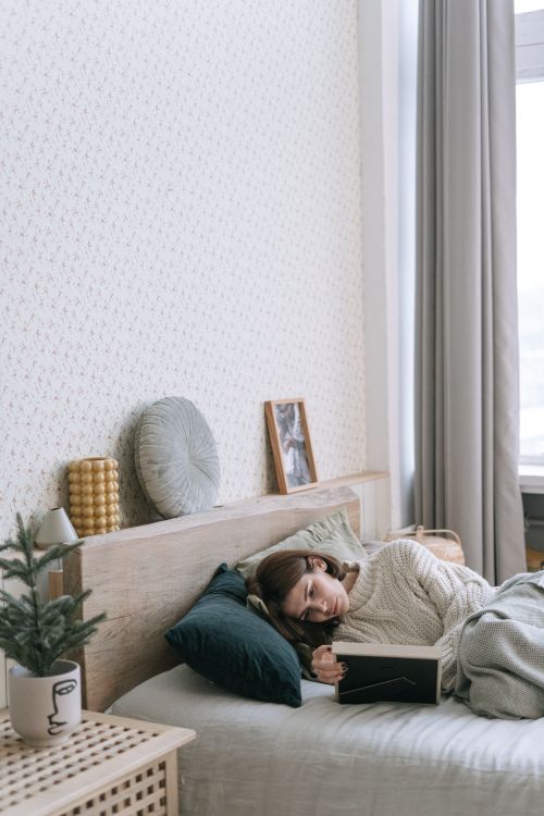 Free A woman relaxing on a bed in a cozy bedroom holding a book, creating a serene indoor ambiance. Stock Photo