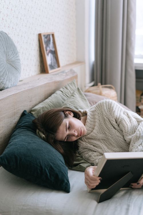 Free A woman in a cozy sweater lies on a bed holding a picture frame in a serene bedroom. Stock Photo