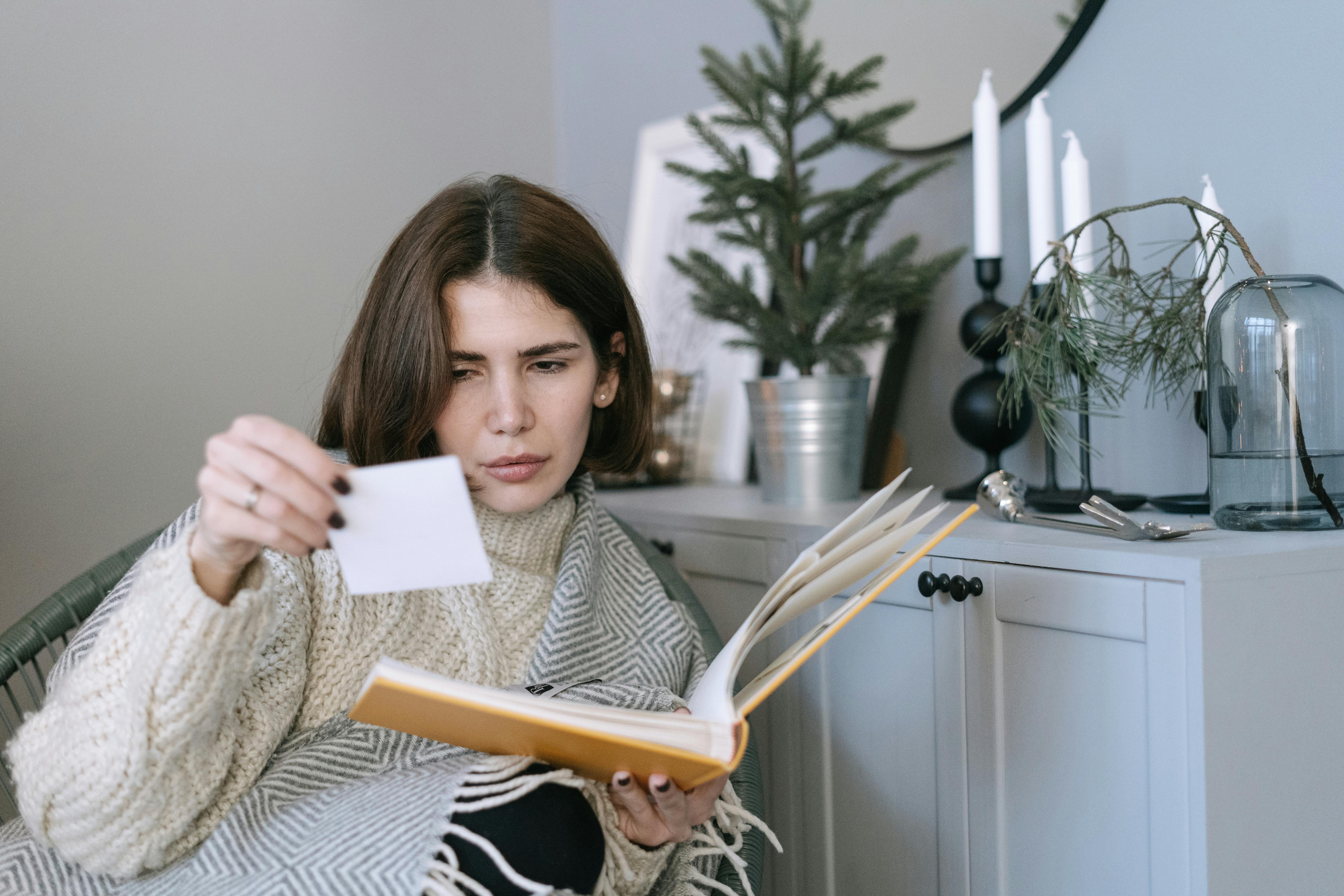 A woman examines a photograph while sitting in a cozy indoor space, surrounded by decor.