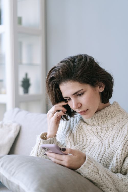Free Woman in a cozy sweater using a smartphone at home, illustrating modern lifestyle. Stock Photo
