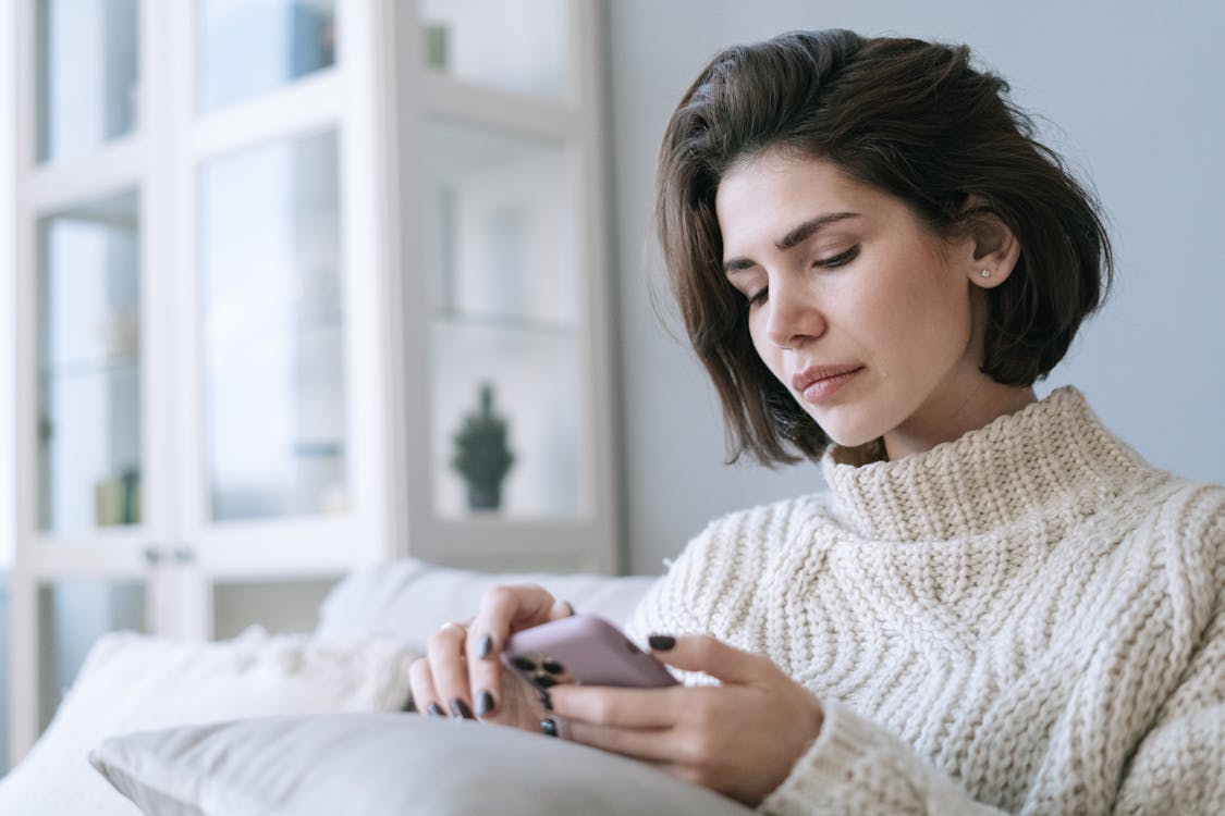 Free A Woman in White Knitted Sweater Using a Cellphone Stock Photo