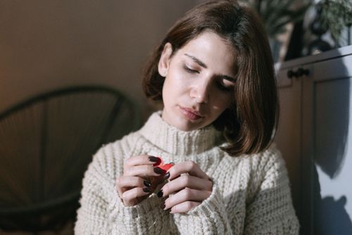 Free A brunette woman holding a red paper heart, looking thoughtful in a cozy indoor setting. Stock Photo