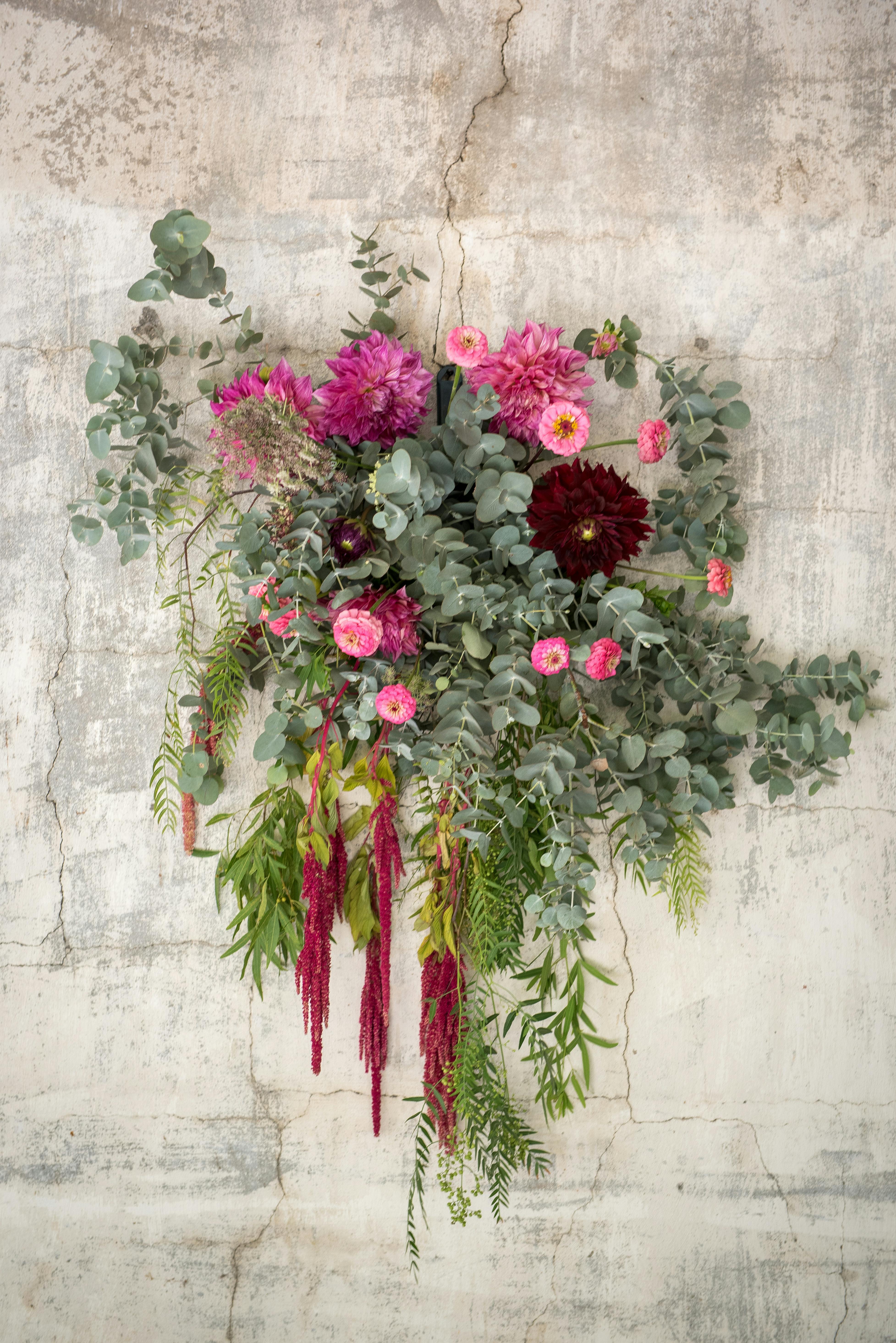 Vibrant floral arrangement with pink and red flowers hanging against a textured wall.