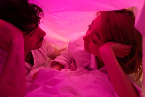 Free Close-up of a couple sharing intimate moment under pink-lit blanket. Stock Photo