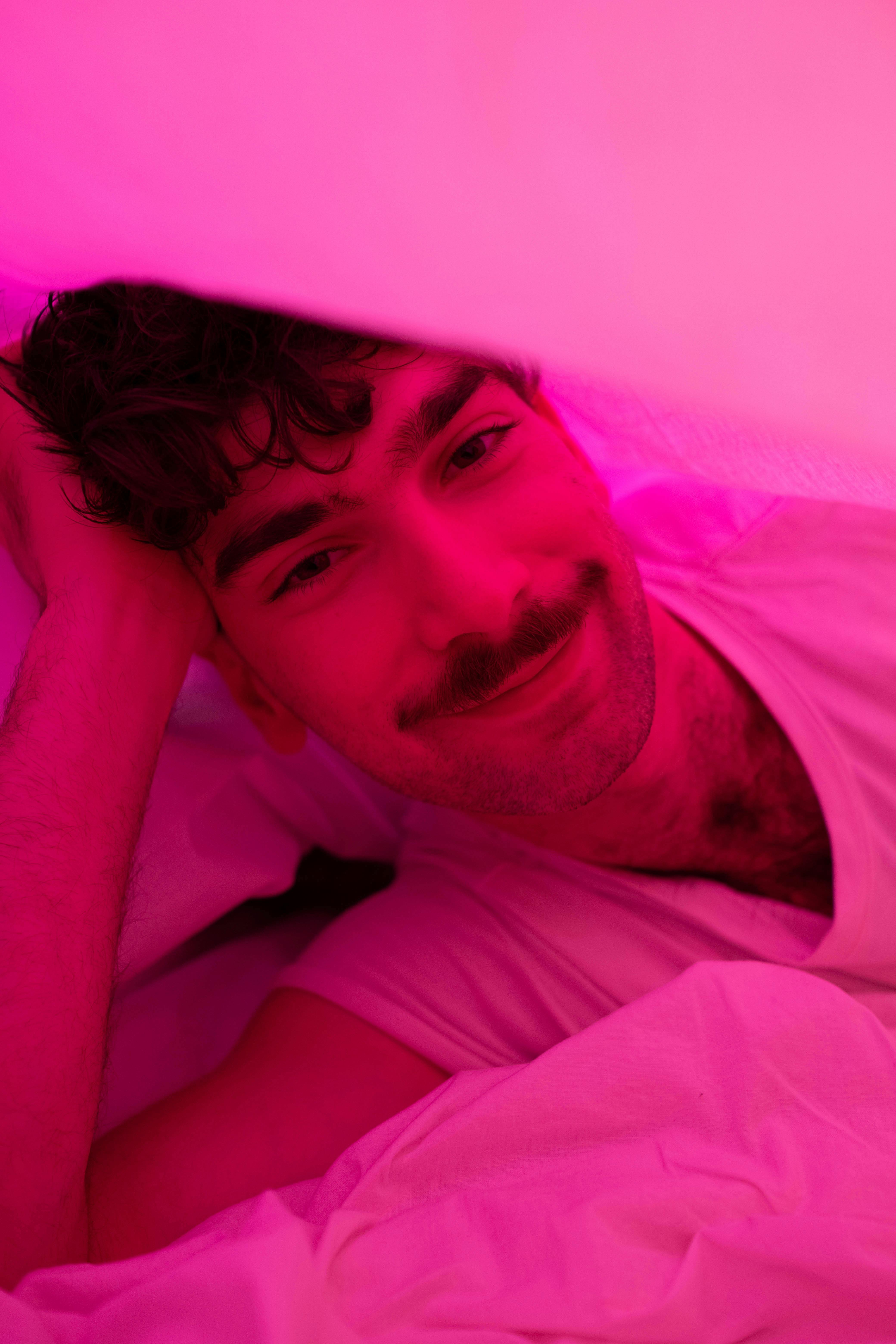A happy, bearded man smiles warmly while relaxed under a pink light.