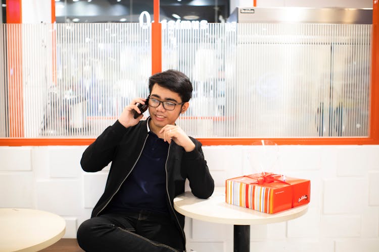 Asian Man Speaking On Smartphone Near Table With Gift Box