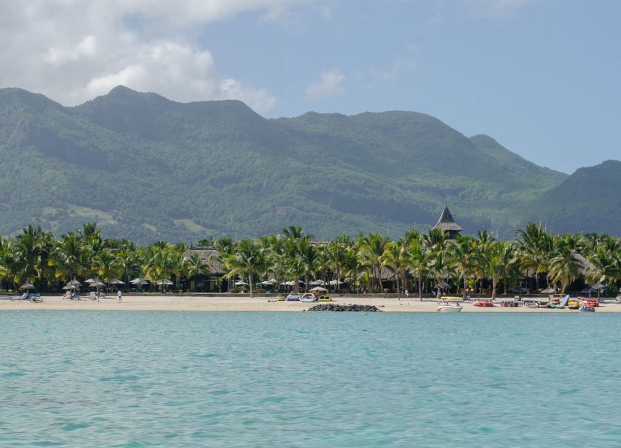 Peaceful tropical beach scene with palm trees, azure sea, and distant mountains.