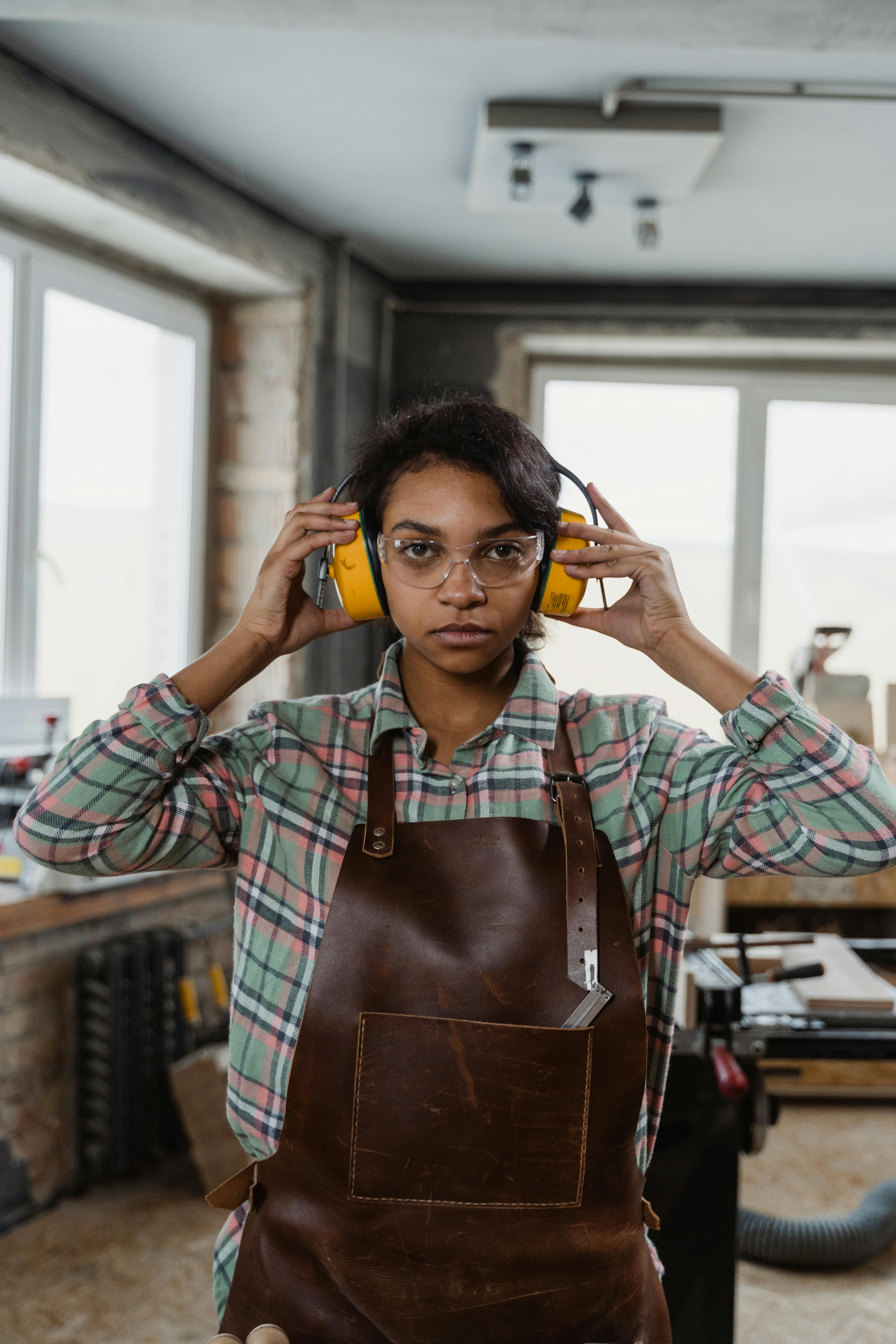 A female woodworker adjusting her ear protection gear in a workshop setting.