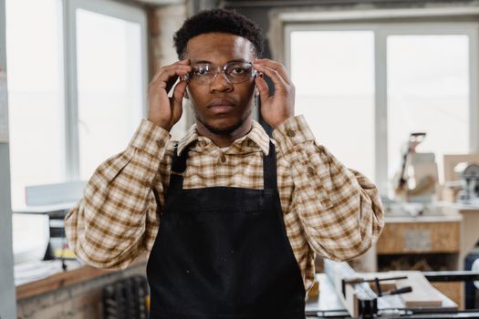 Professional woodworker in workshop wearing apron and glasses, focusing on craftsmanship.