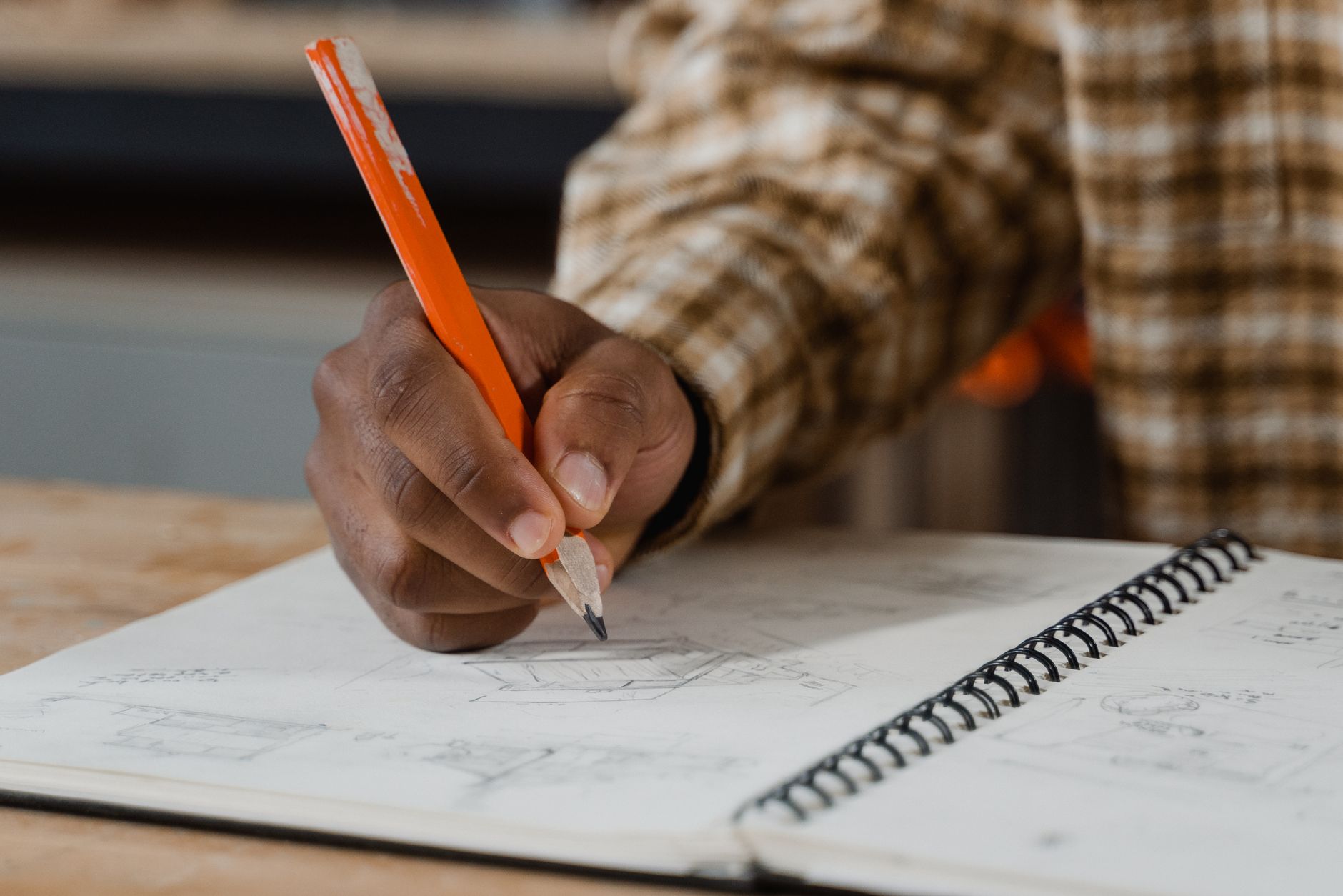 A close-up of a hand drawing in a sketchbook, emphasizing creativity and focus in an indoor workspace.