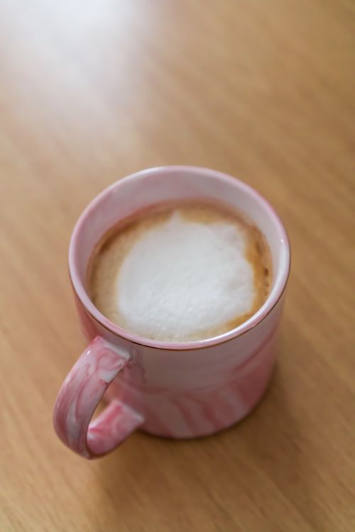 Free A pink marble mug filled with frothy coffee sits elegantly on a wooden table, showcasing a cozy and inviting scene. Stock Photo