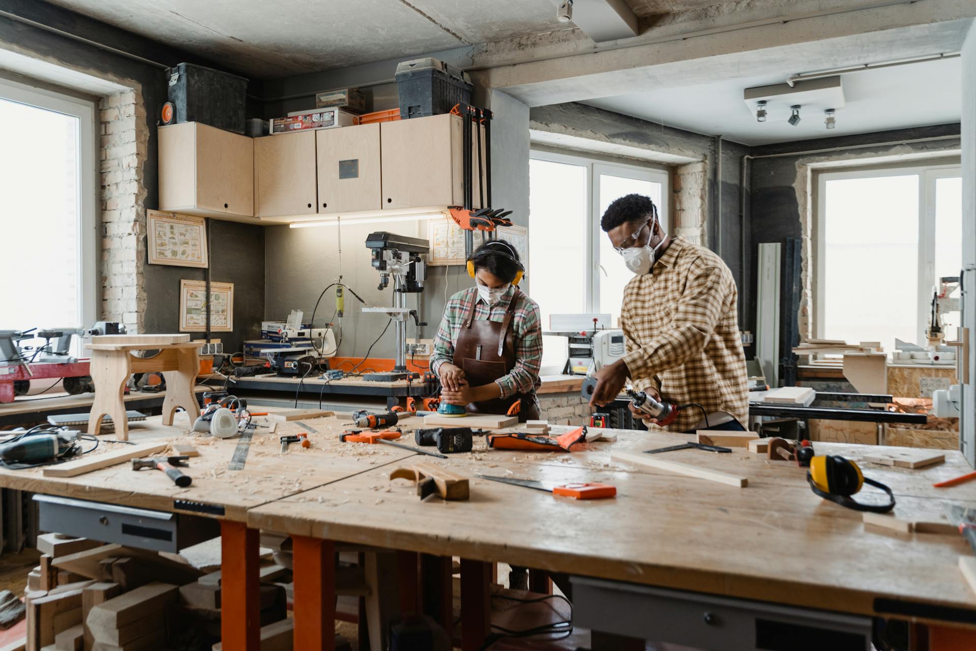 Two artisans working with tools in a well-equipped woodworking studio.