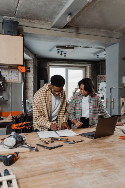 Free Two artisans collaborate in a woodworking workshop. Tools and laptop on the workbench. Stock Photo