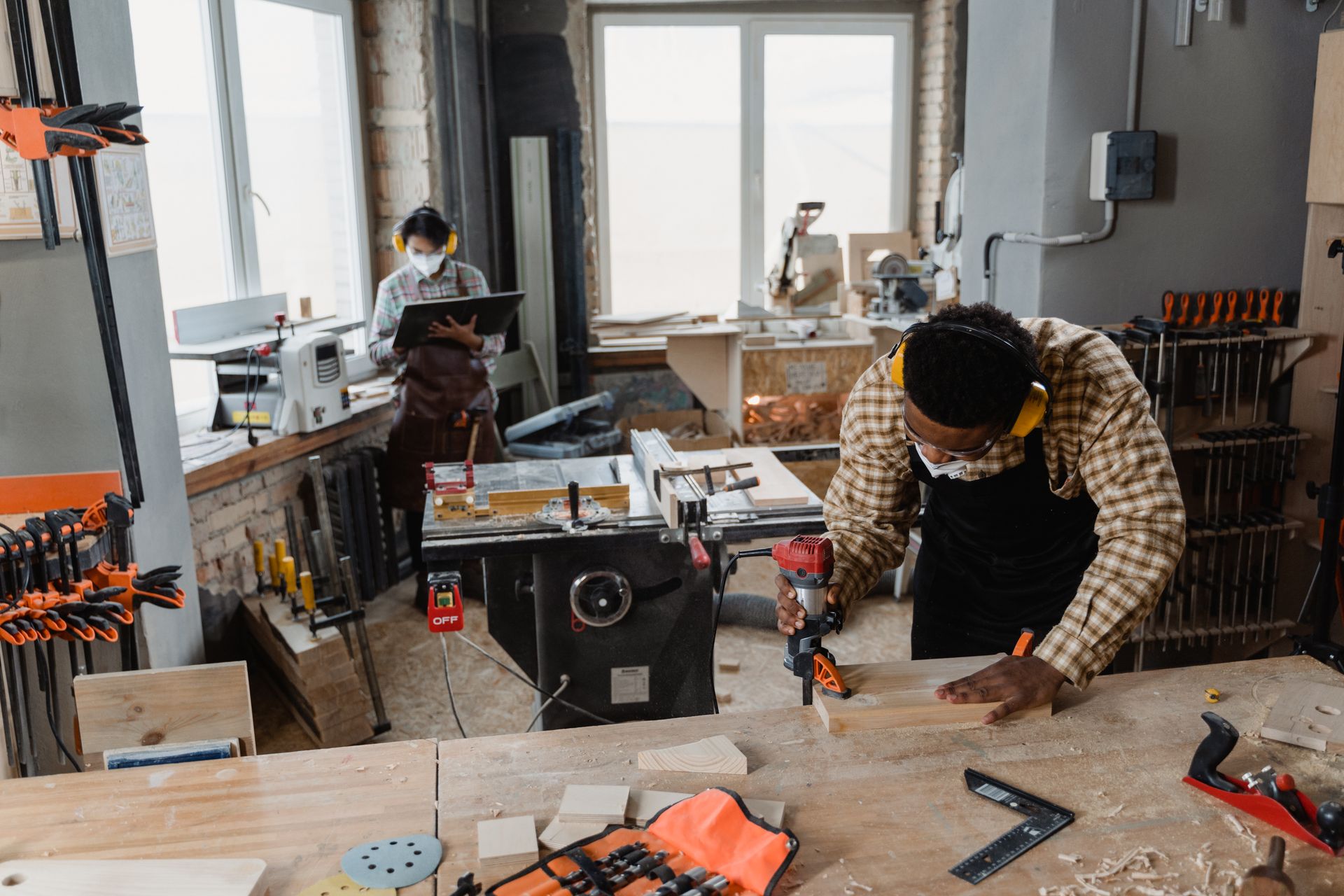 A carpenter using power tools in an indoor woodworking workshop, wearing safety gear.