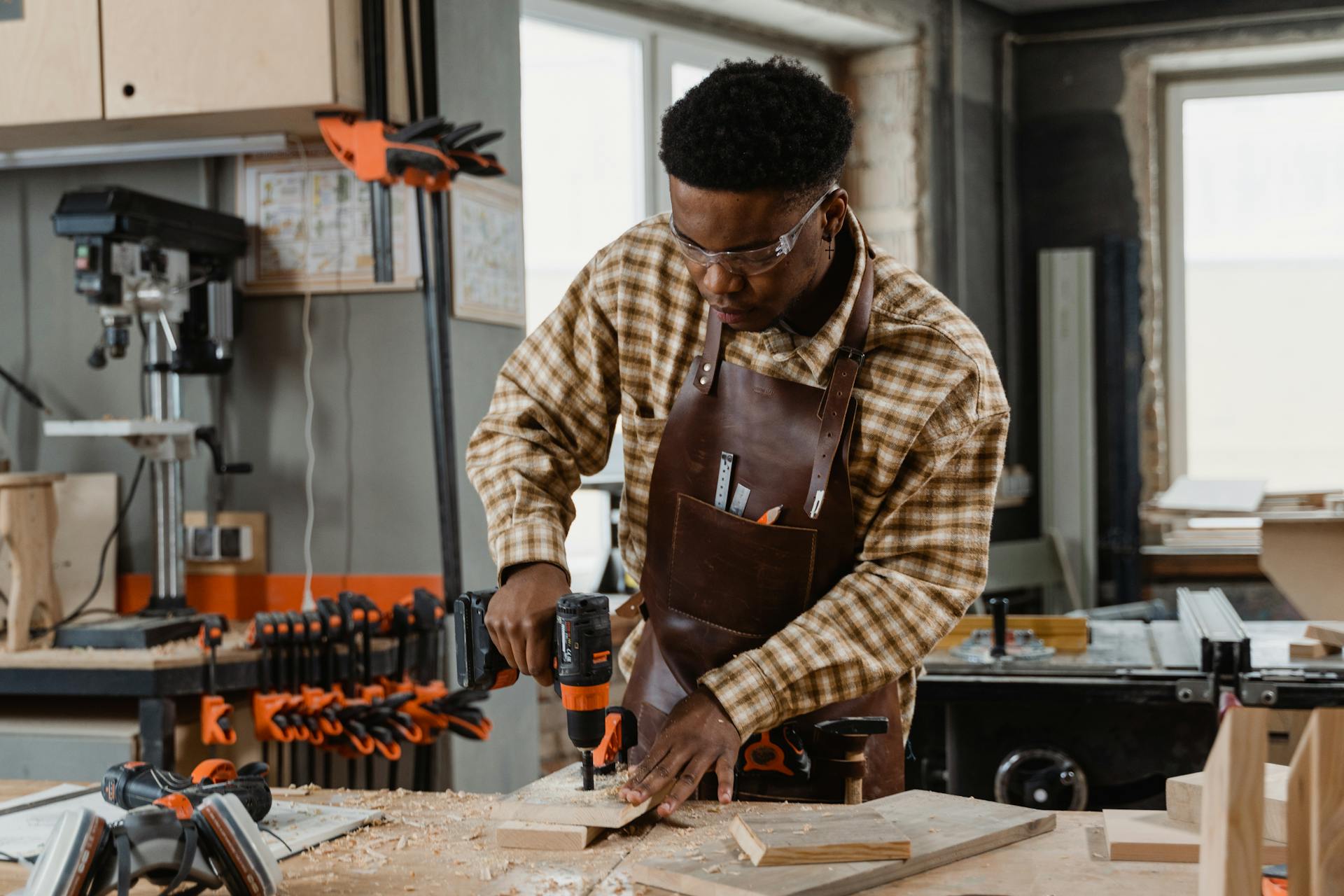 A skilled woodworker in protective gear drills into wood in a workshop setting.