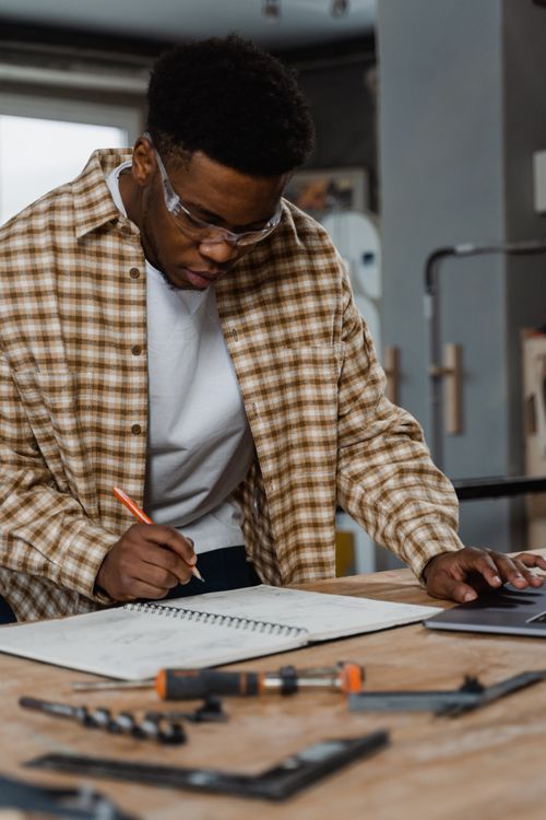Free Skilled craftsman writing notes at a workspace with woodworking tools in view. Stock Photo