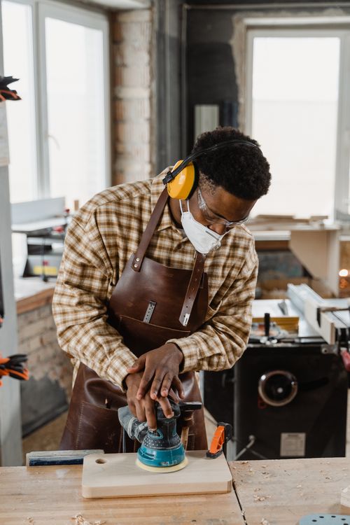 Free African American craftsman using a sander on wood in an indoor workshop setting. Stock Photo