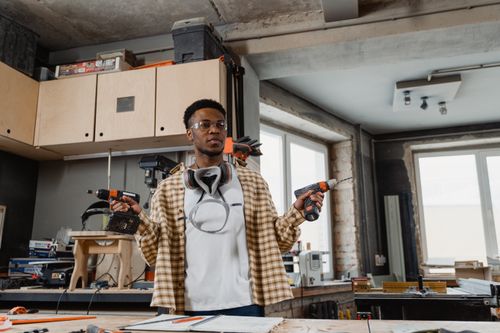Free A young craftsman working in a well-equipped woodworking shop, holding power drills. Stock Photo
