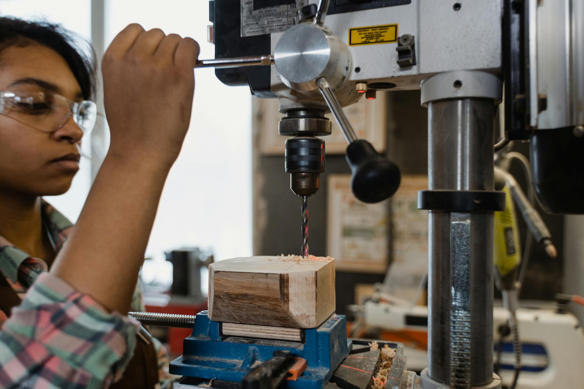 A female carpenter skillfully operating a drill press in a workshop, working on a woodwork project.