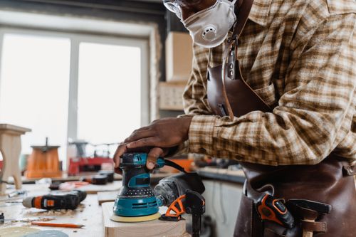 Free Skilled craftsman using an orbital sander on a wooden board in a workshop. Stock Photo